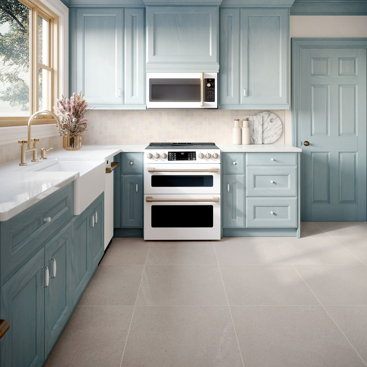 Modern kitchen with light blue cabinets, white double oven, farmhouse sink, and gold faucet under a window.